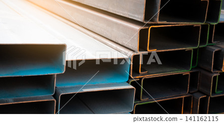 Industrial warehouse stock of rectangular metal pipes for building and construction supplies. Stack of steel pipes. Iron materials for construction and infrastructure projects. Steel tubing storage. Industrial warehouse stock of rectangular metal pipes for building and construction supplies. Stack of steel pipes. Iron materials for construction and infrastructure projects. Steel tubing storage. 141162115