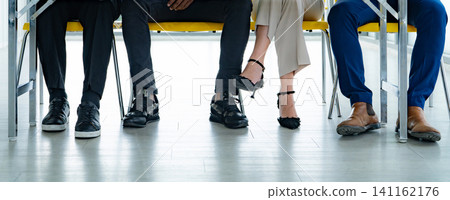Unrecognizable business professionals sitting in a waiting room before a job interview or corporate meeting. Recruitment, diversity, workplace culture, patience, and modern office. Office appointment. 141162176