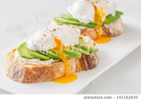 Avocado toast with poached eggs and runny yolk on artisan bread plate Avocado toast with poached eggs and runny yolk on artisan bread plate 141162630