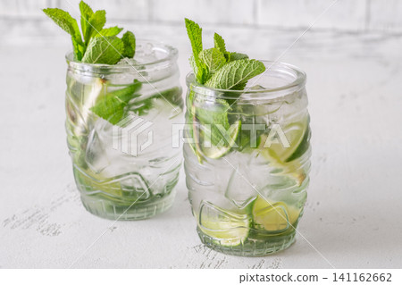 Two fresh mojito cocktails in tiki glasses with lime mint garnish Two fresh mojito cocktails in tiki glasses with lime mint garnish 141162662