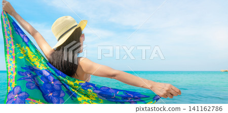 Back view of a woman wearing a straw hat and colorful beach scarf beside a tropical turquoise sea, enjoying a sunny summer vacation, coastal relaxation, wellness, travel freedom, and peaceful island. Back view of a woman wearing a straw hat and colorful beach scarf beside a tropical turquoise sea, enjoying a sunny summer vacation, coastal relaxation, wellness, travel freedom, and peaceful island. 141162786