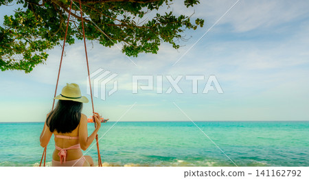 Woman relaxing on a rope swing beneath a tropical seaside tree overlooking the turquoise ocean. Peaceful summer vacation, beach paradise, wellness retreat, and unforgettable coastal travel destination Woman relaxing on a rope swing beneath a tropical seaside tree overlooking the turquoise ocean. Peaceful summer vacation, beach paradise, wellness retreat, and unforgettable coastal travel destination 141162792