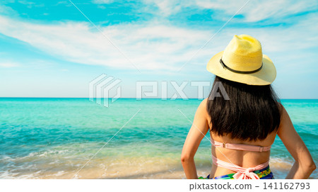 Back view of a woman in a sun hat enjoying a tropical beach with turquoise ocean. Relaxation, wellness, coastal travel, and vacation lifestyle. Beach vacation, mindful travel, summer tourism. Back view of a woman in a sun hat enjoying a tropical beach with turquoise ocean. Relaxation, wellness, coastal travel, and vacation lifestyle. Beach vacation, mindful travel, summer tourism. 141162793