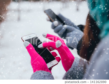 Couple using smartphone in winter with gloves for touch screens Couple using smartphone in winter with gloves for touch screens 141162890