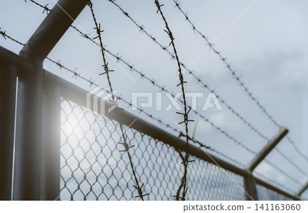 Prison security fence. Border fence. Barbed wire security fence. Razor wire jail fence. Boundary security wall. Prison for arrest of criminals or terrorists. Private area. Military zone concept. Prison security fence. Border fence. Barbed wire security fence. Razor wire jail fence. Boundary security wall. Prison for arrest of criminals or terrorists. Private area. Military zone concept. 141163060