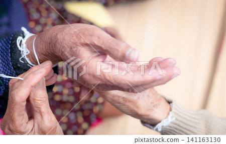 The ceremony of binding elderly people wrist with the holy thread to console old people's Kwan. Thai culture. Beliefs and local culture of Northeastern Thai people. Aging society in Southeast Asia. The ceremony of binding elderly people wrist with the holy thread to console old people's Kwan. Thai culture. Beliefs and local culture of Northeastern Thai people. Aging society in Southeast Asia. 141163130