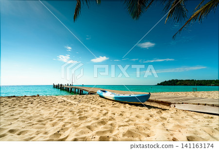 Beautiful view tropical paradise beach of resort. Coconut tree, wooden bridge, and kayak at resort on sunny day. Summer vacation concept. Summer vibes. Golden sand beach of resort with blue sky. Beautiful view tropical paradise beach of resort. Coconut tree, wooden bridge, and kayak at resort on sunny day. Summer vacation concept. Summer vibes. Golden sand beach of resort with blue sky. 141163174