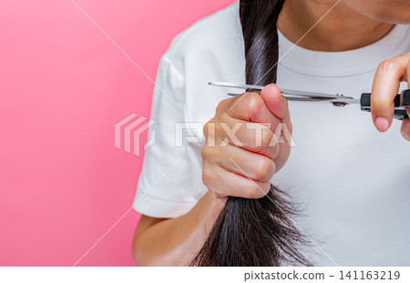 Women cutting damaged and dry hair. Asian woman cutting hair with scissors for donating to cancer patients. Hair donation for breast cancer person. Woman with black long hair on pink background. 141163219