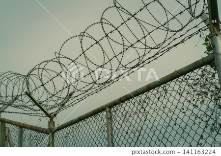 Prison security fence. Barbed wire security fence. Razor wire jail fence. Barrier border. Boundary security wall. Prison for arrest criminals or terrorists. Private area. Military zone concept. Prison security fence. Barbed wire security fence. Razor wire jail fence. Barrier border. Boundary security wall. Prison for arrest criminals or terrorists. Private area. Military zone concept. 141163224