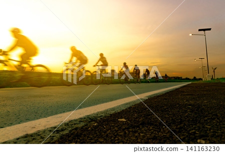 Blur photo sports man ride bicycles with speed motion on the road in the evening with sunset sky. Summer outdoor exercise for healthy and happy life. Cyclist riding mountain bike on bike lane. Team. Blur photo sports man ride bicycles with speed motion on the road in the evening with sunset sky. Summer outdoor exercise for healthy and happy life. Cyclist riding mountain bike on bike lane. Team. 141163230