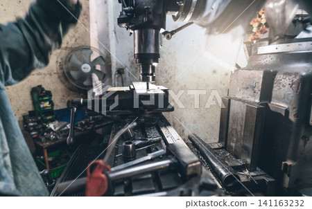 Selective focus on milling machine. Blurred worker is working on milling machine to milling metal plate. Tool for cut metal workpiece. Steel manufacturing factory. Milling process. Machine in workshop Selective focus on milling machine. Blurred worker is working on milling machine to milling metal plate. Tool for cut metal workpiece. Steel manufacturing factory. Milling process. Machine in workshop 141163232