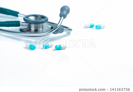 Stethoscope and blue-white capsule pills on doctor table or nurse desk. Health checkup. Medical healthcare and medicine background. Physician tool for patient diagnosis. Cardiology doctor equipment. Stethoscope and blue-white capsule pills on doctor table or nurse desk. Health checkup. Medical healthcare and medicine background. Physician tool for patient diagnosis. Cardiology doctor equipment. 141163736