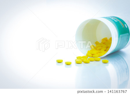 Yellow tablets pills spread out of drug bottle. Tablets pills with bottle on white table. Drug production in pharmaceutical industry concept. Healthcare and medicine background. Medication use. Yellow tablets pills spread out of drug bottle. Tablets pills with bottle on white table. Drug production in pharmaceutical industry concept. Healthcare and medicine background. Medication use. 141163767