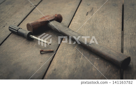 Old rusted hammer, screwdriver and nail on old wooden table. Woodwork tools for fix and repair home. Carpentry tools on an old workbench. DIY tool kit. Equipment for construction in house. Home fix. Old rusted hammer, screwdriver and nail on old wooden table. Woodwork tools for fix and repair home. Carpentry tools on an old workbench. DIY tool kit. Equipment for construction in house. Home fix. 141163782