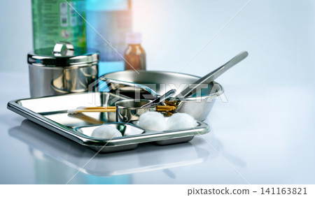 Wound care dressing set on stainless steel plate. White cotton ball, cotton stick, forceps, alcohol, iodine cup, instruments container  with cover or stainless steel cotton jar set. Medical tool. 141163821