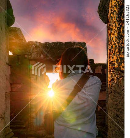 Rearview of woman photographer travel in Phimai Historical Park with sunset sky. Landmark of Nakhon Ratchasima, Thailand. Travel destinations. Historic site is ancient. Ancient building. Khmer temple. 141163822