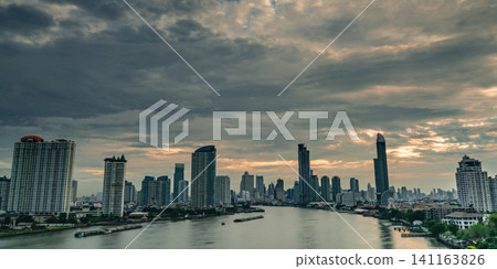 Cityscape of modern building near the river in the morning with orange sunrise sky and clouds at Bangkok in Thailand. Modern architecture office building. Skyscraper with morning sky and Ferris wheel. Cityscape of modern building near the river in the morning with orange sunrise sky and clouds at Bangkok in Thailand. Modern architecture office building. Skyscraper with morning sky and Ferris wheel. 141163826