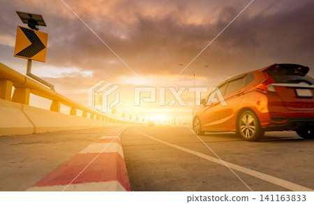 Motion blur of red car driving on curve concrete road with a traffic sign. Road trip on summer vacation. Car drive on the street. Summer travel by car. Solar panel energy on yellow curve traffic sign Motion blur of red car driving on curve concrete road with a traffic sign. Road trip on summer vacation. Car drive on the street. Summer travel by car. Solar panel energy on yellow curve traffic sign 141163833