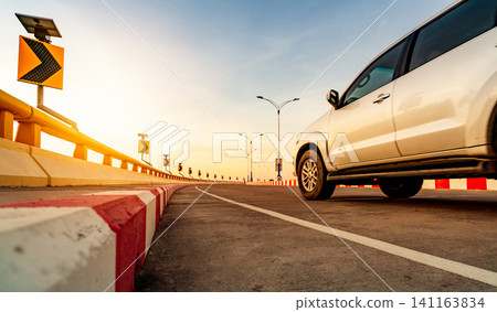 Curve concrete road with curve traffic sign and red-white prohibited stop sign. Solar panel energy on curve traffic sign. Road trip. Motion blur of white car driving on the road. Road trip on summer. Curve concrete road with curve traffic sign and red-white prohibited stop sign. Solar panel energy on curve traffic sign. Road trip. Motion blur of white car driving on the road. Road trip on summer. 141163834