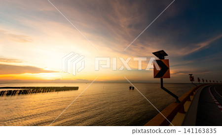 View from curve road to sunset skyline over the tropical sea in Thailand. Calm sea with yellow sunset sky. Beauty in nature. Road beside the sea in summer. Summer road trip travel concept. Tranquility View from curve road to sunset skyline over the tropical sea in Thailand. Calm sea with yellow sunset sky. Beauty in nature. Road beside the sea in summer. Summer road trip travel concept. Tranquility 141163835