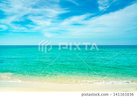 Golden sand beach by the sea with emerald green sea water and blue sky and white clouds. Summer vacation on tropical paradise beach concept. Ripple of water splash on sandy beach. Summer vibes. Golden sand beach by the sea with emerald green sea water and blue sky and white clouds. Summer vacation on tropical paradise beach concept. Ripple of water splash on sandy beach. Summer vibes. 141163836