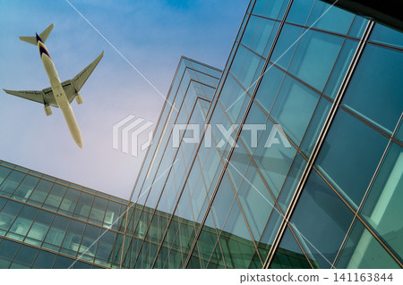Airplane flying above office building. Skyscraper modern building. Finance business trip. Glass windows. Aviation business after coronavirus vaccine injection. Plane flying above futuristic building. Airplane flying above office building. Skyscraper modern building. Finance business trip. Glass windows. Aviation business after coronavirus vaccine injection. Plane flying above futuristic building. 141163844