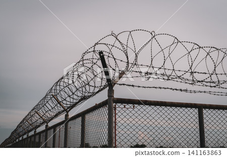 Prison security fence. Barbed wire security fence. Razor wire jail fence. Barrier border. Boundary security wall. Prison for arrest criminals or terrorists. Private area. Military zone concept. Prison security fence. Barbed wire security fence. Razor wire jail fence. Barrier border. Boundary security wall. Prison for arrest criminals or terrorists. Private area. Military zone concept. 141163863