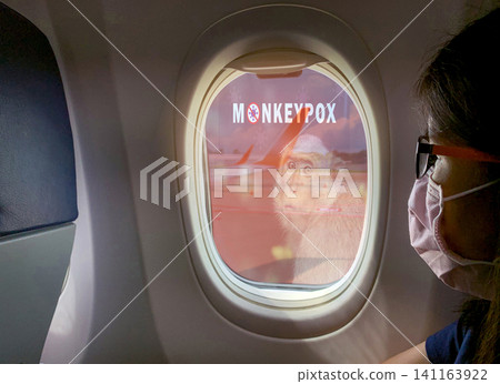 Woman wear surgical mask sit on passenger seat near cabin window of the airplane with monkeypox outbreak concept. Monkeypox is caused by monkeypox virus. Traveling by plane during monkeypox outbreak. 141163922