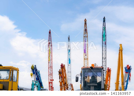 Close-up mobile crane, yellow bulldozer, and blue backhoe parked at second-hand machinery auction yard against blue sky. Heavy machinery for rent and sale. Crane dealership for construction business. 141163957