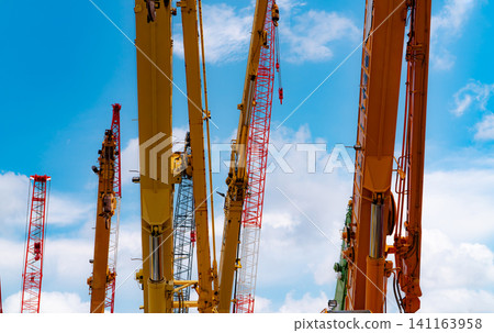Crawler crane against blue sky and white clouds. Real estate industry. Red crawler crane use reel lift up equipment in construction site. Crane for rent. Crane dealership for construction business. Crawler crane against blue sky and white clouds. Real estate industry. Red crawler crane use reel lift up equipment in construction site. Crane for rent. Crane dealership for construction business. 141163958