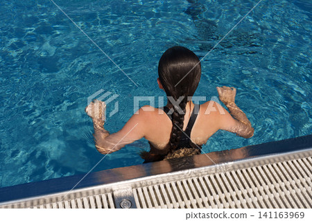 Teen girl holding pool edge after swimming in outdoor pool 141163969