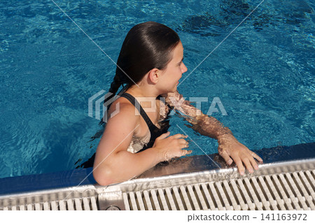 Teen girl holding pool edge after swimming in outdoor pool Teen girl holding pool edge after swimming in outdoor pool 141163972