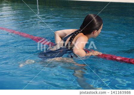 Teen girl holding red lane rope while swimming in outdoor pool Teen girl holding red lane rope while swimming in outdoor pool 141163986