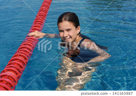 Teen girl holding red lane rope while swimming in outdoor pool Teen girl holding red lane rope while swimming in outdoor pool 141163987