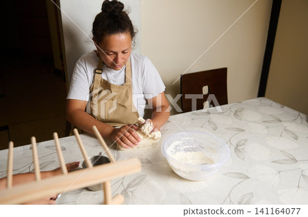 Woman kneading dough at kitchen table preparing homemade bread 141164077