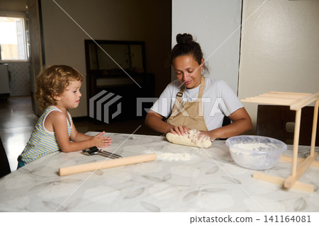 Mother and child baking bread together in home kitchen, kneading dough and sharing a warm moment 141164081