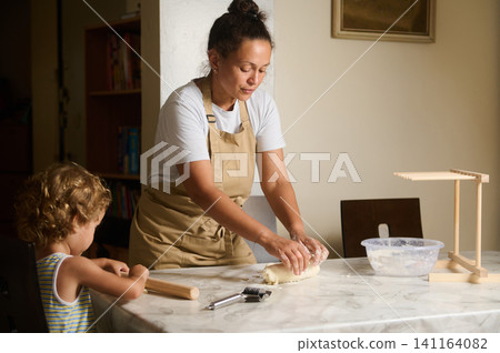 Mother and child baking dough together at home kitchen, hands kneading and learning Mother and child baking dough together at home kitchen, hands kneading and learning 141164082