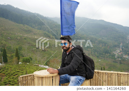 Young Indian male traveler sitting on a bamboo deck overlooking the scenic tea gardens of Tinchuley Darjeeling Young Indian male traveler sitting on a bamboo deck overlooking the scenic tea gardens of Tinchuley Darjeeling 141164260