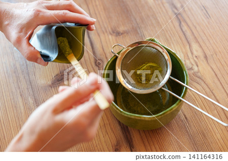 Sifting matcha powder into bowl for homemade iced latte recipe Sifting matcha powder into bowl for homemade iced latte recipe 141164316