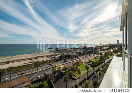 Panoramic coastal cityscape with sandy beach, palm trees, clear blue sky, distant buildings, and gentle ocean waves beside shoreline, with beach, coast, ocean, sand detail Panoramic coastal cityscape with sandy beach, palm trees, clear blue sky, distant buildings, and gentle ocean waves beside shoreline, with beach, coast, ocean, sand detail 141164520