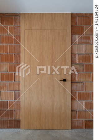 Plain wooden door set in textured red brick wall with dark handle and minimalist design Plain wooden door set in textured red brick wall with dark handle and minimalist design 141164524