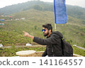 Young Indian male traveler pointing towards scenic tea gardens at Tinchuley in Darjeeling 141164557