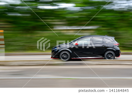 A black compact car speeds through the fresh greenery. 141164845