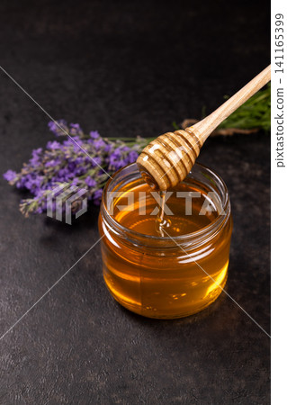 Golden honey dripping from dipper in jar with lavender Golden honey dripping from dipper in jar with lavender 141165399