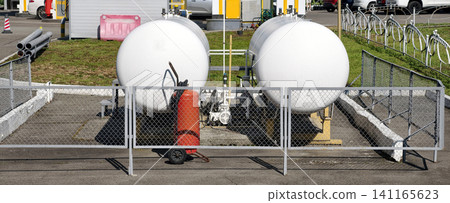 Two metallic fuel containers for liquefied gas connected to industrial pipelines at a gas station with a red fire extinguisher nearby Two metallic fuel containers for liquefied gas connected to industrial pipelines at a gas station with a red fire extinguisher nearby 141165623