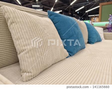 A modern beige sofa with a mix of beige and blue cushions, available for sale in a furniture store A modern beige sofa with a mix of beige and blue cushions, available for sale in a furniture store 141165660