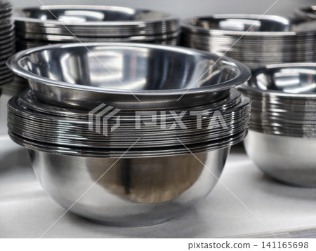 Stacked polished metal bowls on supermarket shelves, reflecting bright lighting and presenting modern stainless steel kitchenware for retail sale in organized store environment Stacked polished metal bowls on supermarket shelves, reflecting bright lighting and presenting modern stainless steel kitchenware for retail sale in organized store environment 141165698