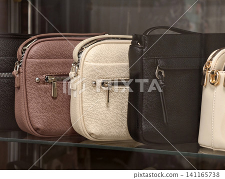 Assorted leather handbags in different colors displayed neatly behind a store window Assorted leather handbags in different colors displayed neatly behind a store window 141165738