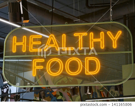 Yellow Healthy Food neon light enhances visual appeal of supermarket interior. Healthy Food neon sign provides bright glow in a grocery store environment Yellow Healthy Food neon light enhances visual appeal of supermarket interior. Healthy Food neon sign provides bright glow in a grocery store environment 141165806