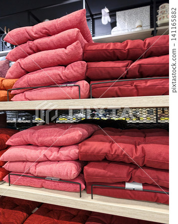 Red seat cushions displayed on supermarket shelves with neatly arranged soft chair pads and vibrant home textile comfort accessories in retail store interior 141165882